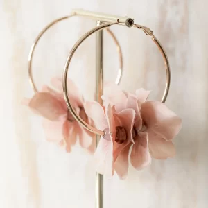 Un par de aretes de aro de flores rosas sobre un soporte de metal.